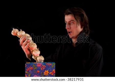 Shocked vampire with gift box taking out garlic, isolated on black background