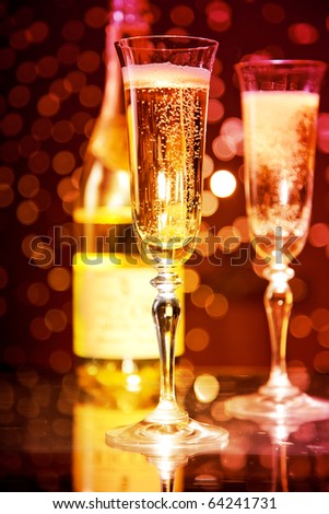 Champagne glasses and bottle over holiday bokeh background, focus on first glass