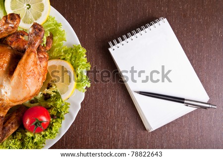 Restaurant table with roast chicken, notebook and pen, ready for order