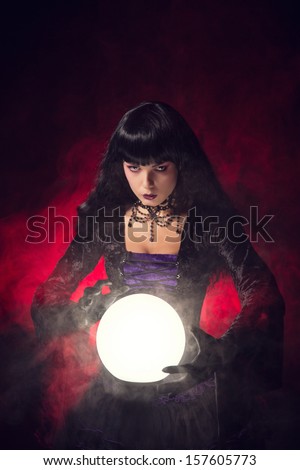 Beautiful gothic style fortune teller with a crystal ball, studio shot over smoky background