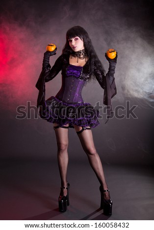 Beautiful witch in purple and black gothic fantasy Halloween costume with Jack lantern oranges