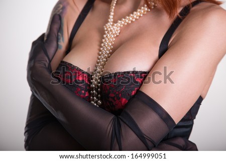 Close-up shot of a busty woman in vintage red bra, sheer gloves and pearl necklace
