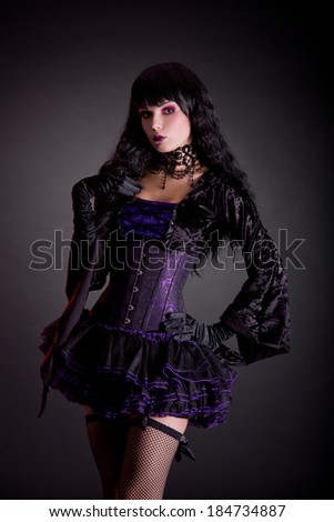 Beautiful witch in purple and black gothic Victorian outfit, studio shot on black background