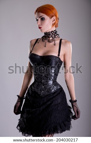 Pretty redhead young woman in silver corset and black skirt, studio shot