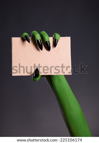 Green skin hand with sharp nails holding empty piece of cardboard, Halloween theme