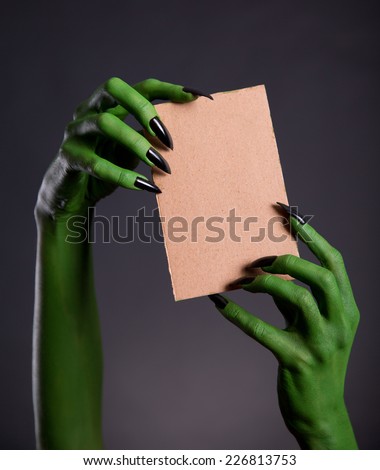 Green monster hands holding empty piece of cardboard, Halloween theme