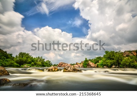 Beautiful river flow with sky stormy clouds, boulders in moving water - long exposure