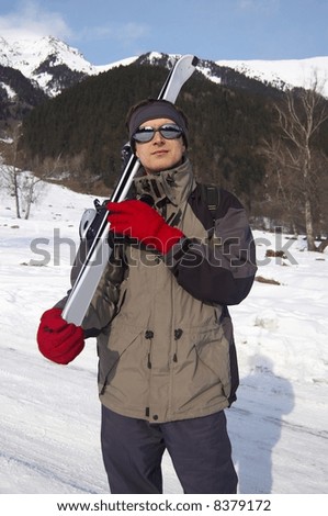 Man in ski clothes taking white skis on his shoulder on a mountain background