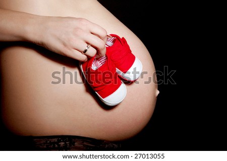 Pregnant woman\'s belly on black background  and hand with baby\'s bootee on belly