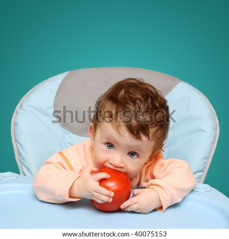 small baby sitting on chair biting tomato