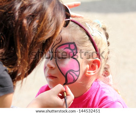 artist paints butterfly on face of cute little girl