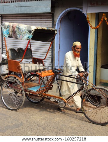 AGRA, INDIA - NOVEMBER 16, 2012: Old indian man rickshaw rolls his bike on street in Agra, India, 16 nov 2012