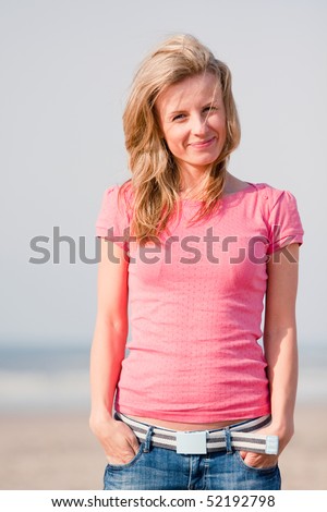 Young woman in pink t-shirt and jeans standing on sea shore. Sunset light