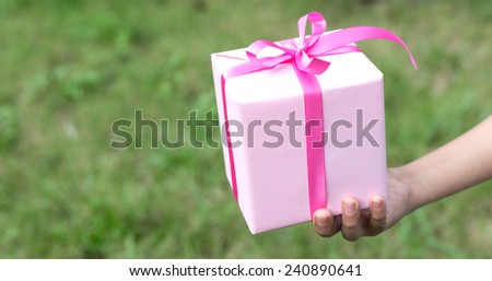 Young boy hand hold pink gift box against nature background