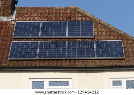 Solar photovoltaic panel array mounted on a tiled house roof against a blue sky