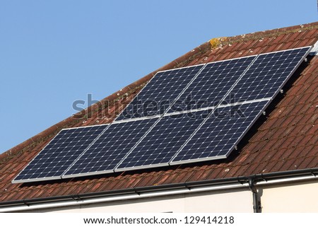 Solar photovoltaic panel array mounted on a tiled house roof against a blue sky