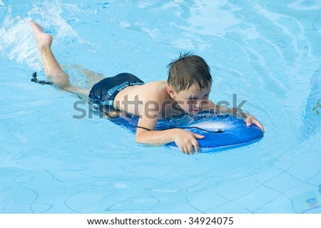 Boy in the swimming-pool. Child floating on a board.