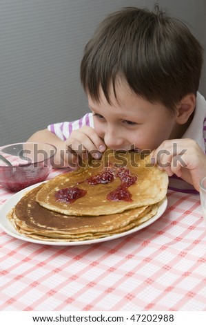Boy eats pancakes with crimson jam.