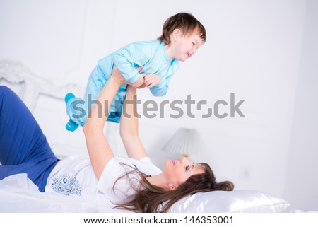 Happy Mom and son playing and laughing in their pajamas on the bed