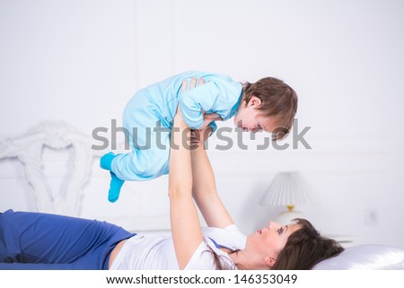 Happy Mom and son playing and laughing in their pajamas on the bed