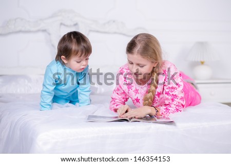 Brother and sister reading a book in bed