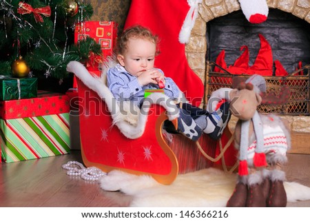 Beautiful curly-haired boy in a sleigh in the New Year fire