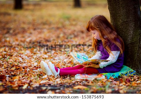 girl in autumn park sitting near a tree on a blanket and reading a book. finger points to the text