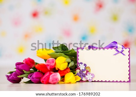 Spring flower arrangement and a greeting card on a wooden table against  wall, text space