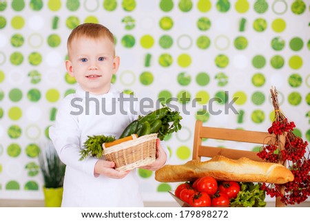 small child in an apron with vegetables and herbs. cucumbers. cook. kitchen, boy chef