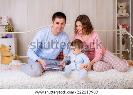 happy parents read a book your child in the nursery. all dressed in pajamas
