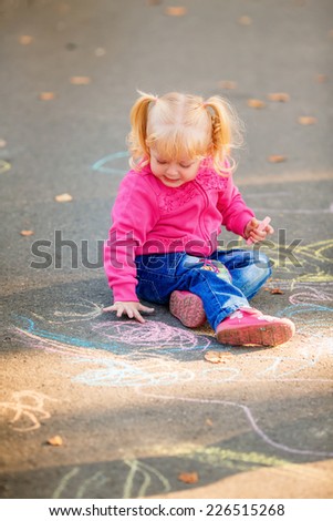 happy little girl draw with crayons on the pavement in the park