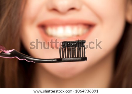 young woman holding a black tooth paste with active charcoal, and black tooth brush on white background
