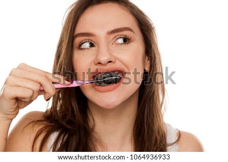 young woman brushing her teeth with a black tooth paste with active charcoal, and black tooth brush on white background