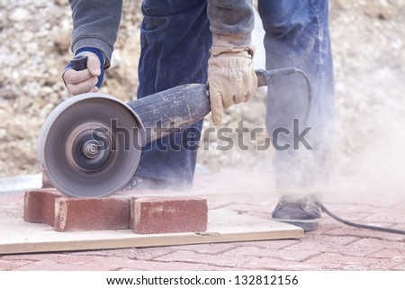 worker uses a stone cutter to cut the brick pavers