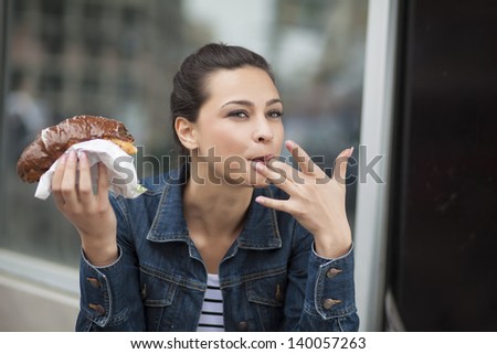 hungry girl eating a donut with chocolate and sucking her finger