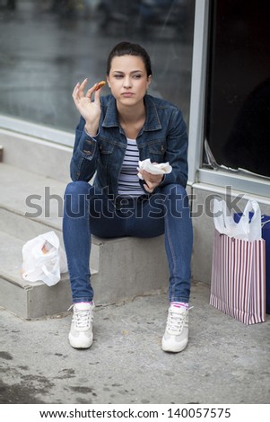 hungry girl eating a donut with chocolate on the stairs to the sidewalk