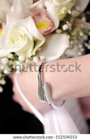 bracelet made of white gold and jewels in the women\'s hand that holds the Biedermeier of roses and orchids