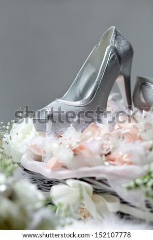 silver women\'s shoe with high heels, put on a basket with flowers