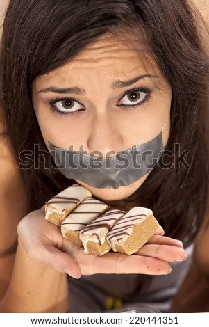 sad girl with adhesive tape over her mouth holding cakes in hand