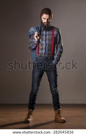 a young man with a beard wearing a denim jacket and jeans posing in studio