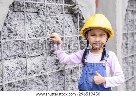 Kid civil engineer inspecting wire mesh on huge concrete pipe wall with hand thumb up