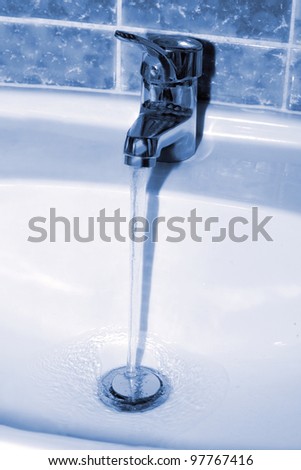 Water tap with a water stream. Blue tone image
