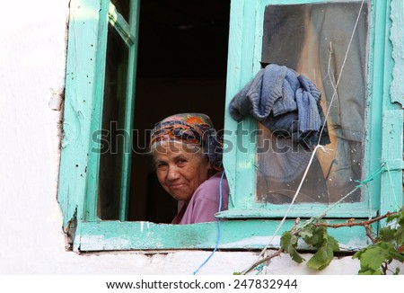 FETHIYE, TURKEY - JUL 8, 2012: Elderly turkish woman looking through the window of old house