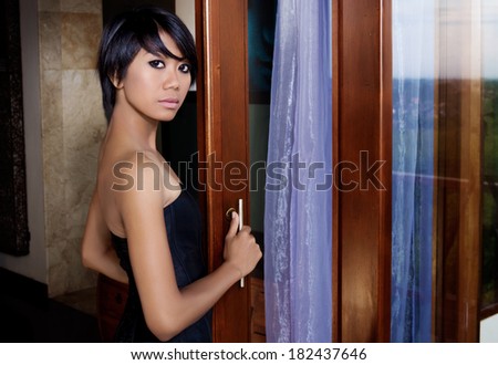 Asian woman stands near the sliding door, bare shoulders and back. reflected in the island of Bali and the bay