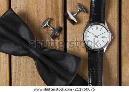 Directly above view of a old wooden table, bowtie cufflinks and wristwatch on it