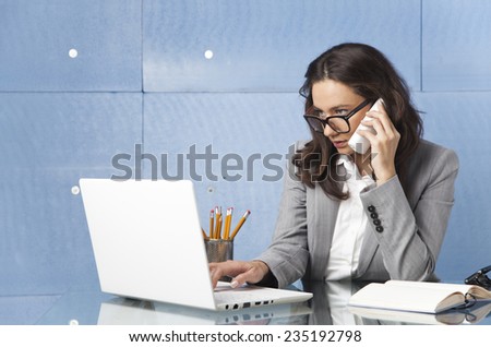 Businesswoman speaking on the phone while typing on keyboard and looking at laptop