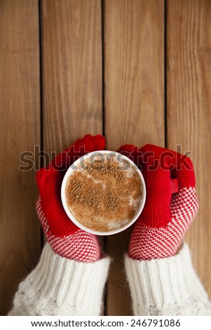 Hands in gloves holding hot cup of coffee