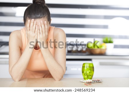 Young woman feeling bad and pills on table