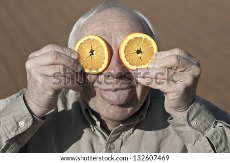Elderly man make funny face with orange slices and his tongue sticks out