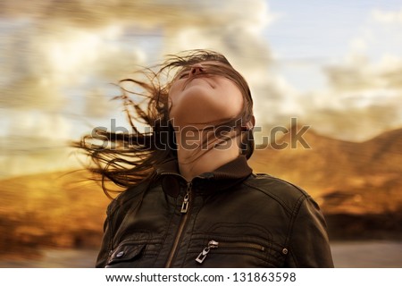 Woman with hair blowing in the wind breathing deeply and looking up wearing a leather jacket with a blurred nature background